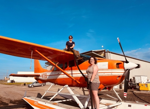 one person sitting on top of and a second person standing in front of an airplane