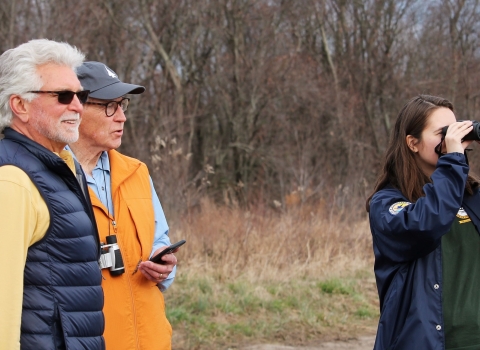 A woman looks through binoculars while two others look on.