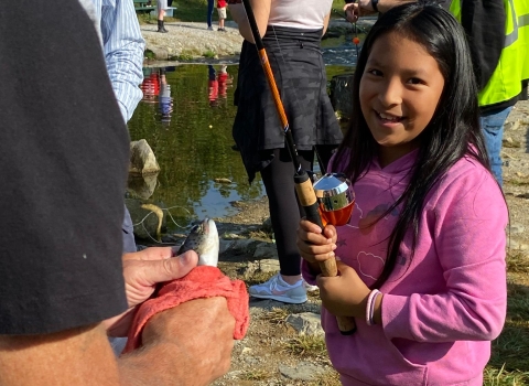 Little girl smiling with a fishing pole in front of a stream