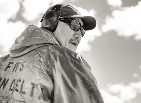 Non-color close up image of Chris Tulik wearing ear protection and sunglasses as he operates a watercraft on the Yukon River. 