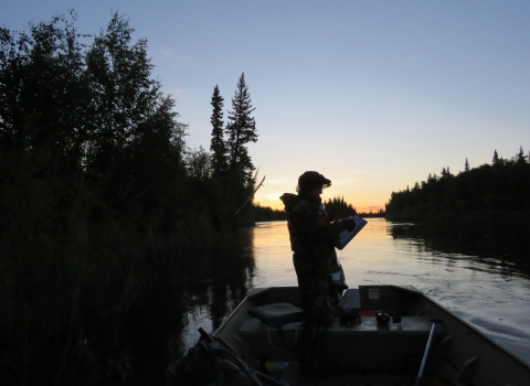 Silhouette of a person in a boat on a river at sunrise