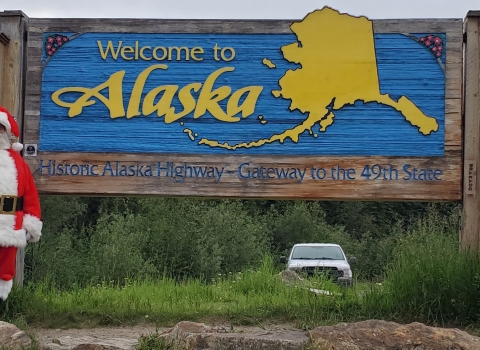 Watercraft inspector, Steve Wogtech, posed in Santa suit in front of Welcome to Alaska sign.