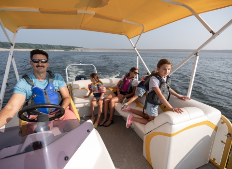 Family wearing lifejackets enjoys a pontoon boat ride on lake. 